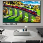 Телевизор LG Micro RGB evo AI показывает пейзаж с поездом в современном интерьере.