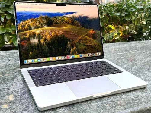 Ноутбук на столе с включенным экраном, демонстрирующий пейзаж с горами и лесом.