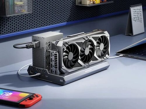 Видеокарта на столе подключена к ноутбуку, рядом игровая консоль.