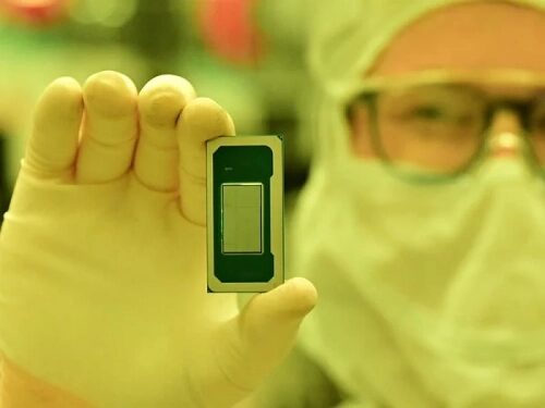 Человек в защитной одежде держит компьютерный чип в лаборатории.