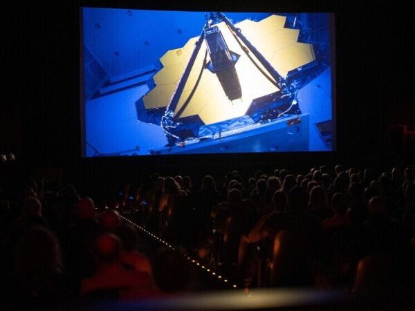 Зрители в кинотеатре смотрят фильм о космическом телескопе Джеймса Уэбба.