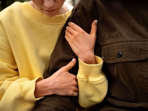 Человек в желтой толстовке обнимает другого в коричневой куртке, выражая близость и поддержку.