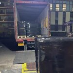 Погрузка черных паллет ночью в грузовик у склада.