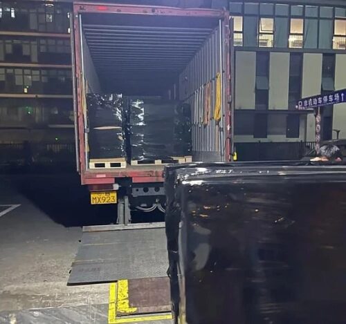 Погрузка черных паллет ночью в грузовик у склада.