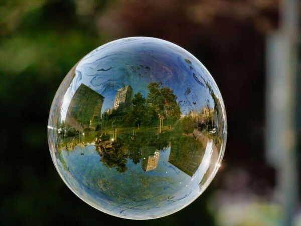 Мыльный пузырь отражает городские здания и деревья, фон размыт.