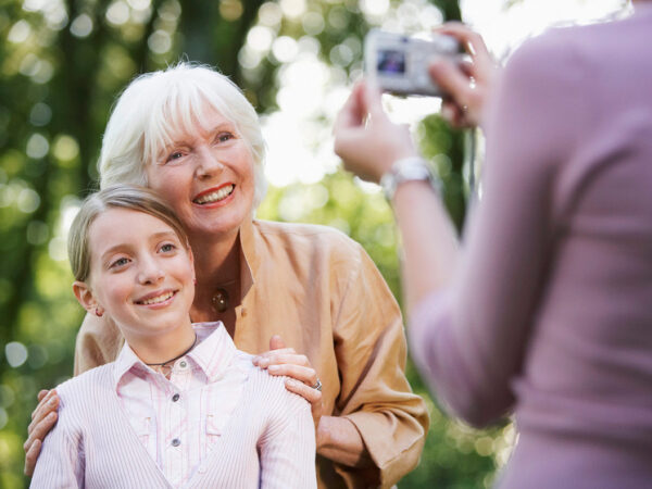Бабушка и внучка позируют для фото на природе, улыбаются и обнимаются.