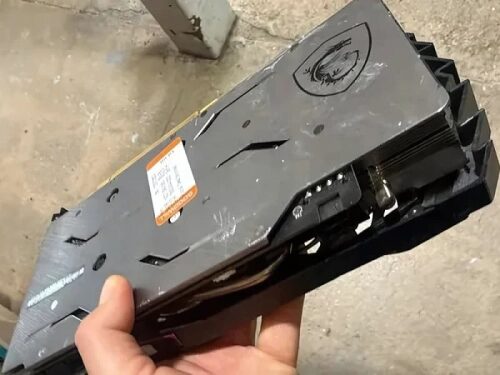 Подержанная видеокарта MSI на сером фоне, сбоку в руке.