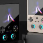 Два портативных ретро-геймпада черного и белого цветов на сером фоне.