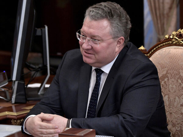 Мужчина в костюме сидит за столом и улыбается.