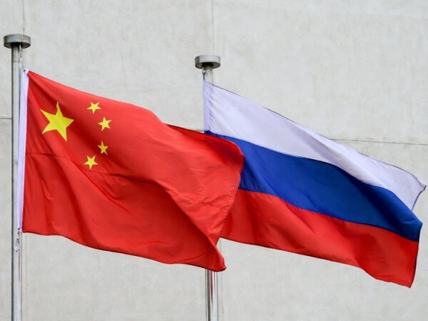 Флаги Китая и России, развевающиеся на ветру на фоне бетонной стены.