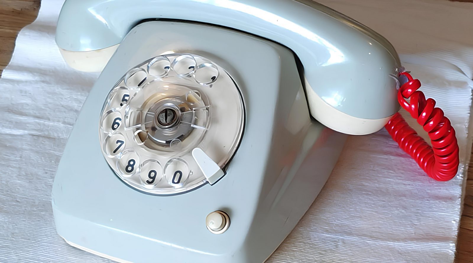 Старый дисковый телефон с красной трубкой на белой поверхности.