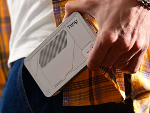 Человек держит в руке мини-компьютер Tiiny у пояса, желтая клетчатая рубашка.