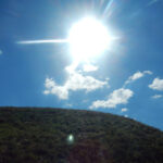 Яркое солнце в голубом небе над зеленым холмом и облаками.