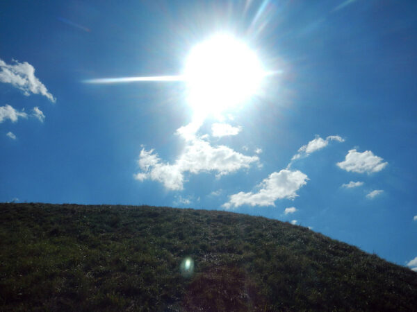 Яркое солнце в голубом небе над зеленым холмом и облаками.