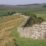 Каменная стена на фоне зелёных холмов и пастбищ, пейзаж в сельской местности.