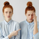 Две девушки с рыжими волосами в голубых рубашках, одна показывает на другую пальцем.