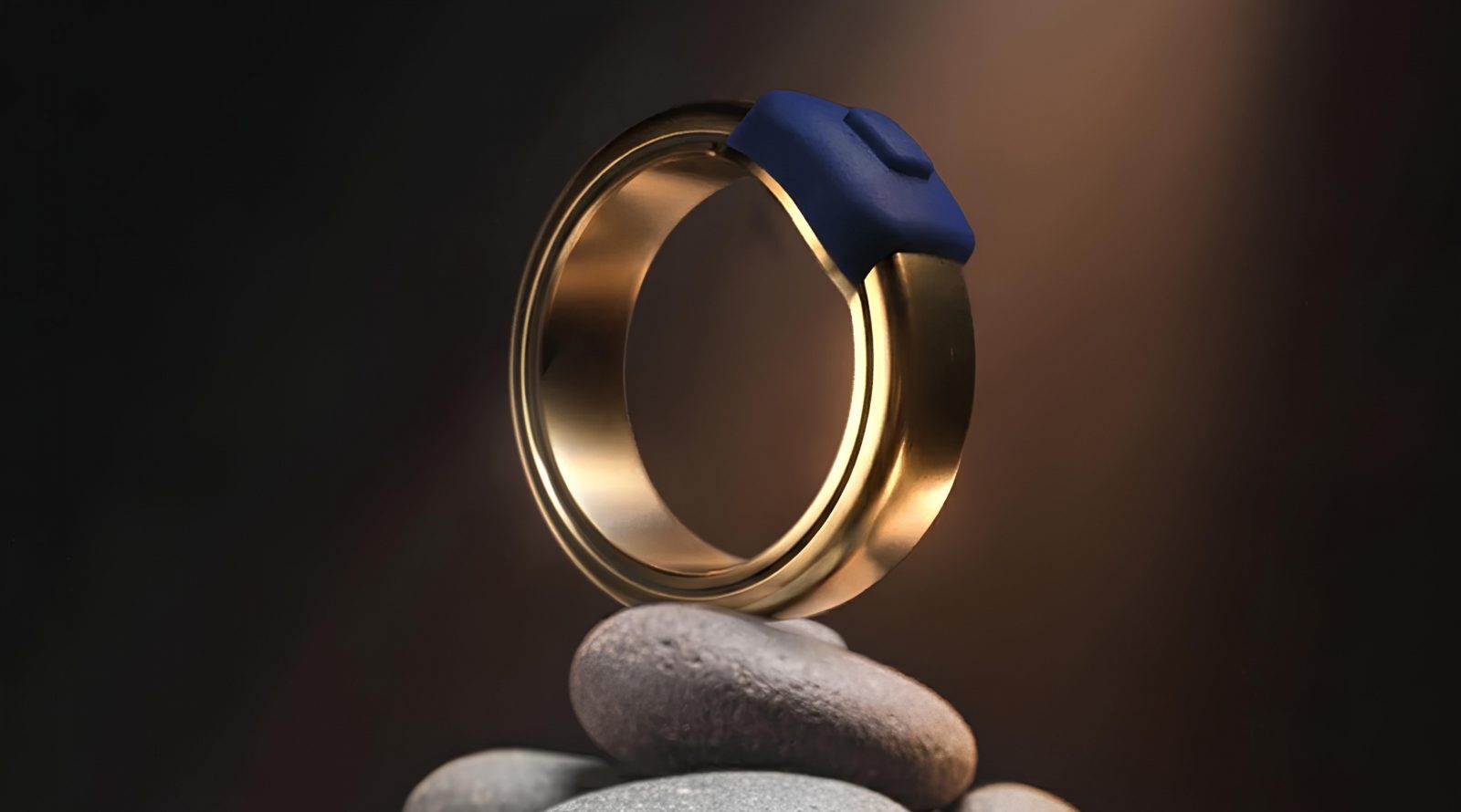 Золотое кольцо с синим элементом на фоне темной композиции из камней.