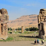 Колоссы Мемнона в Египте, древние статуи фараона Аменхотепа III, туристы на фоне памятника.
