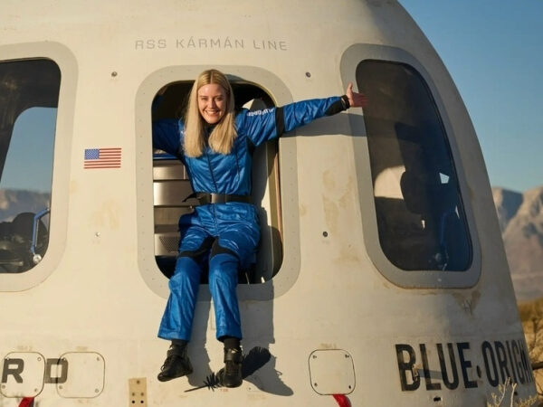 Человек в синем комбинезоне сидит в люке капсулы Blue Origin, руки разведены в стороны.