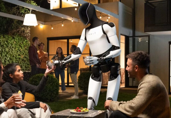 Робот на открытой вечеринке подает напиток, люди общаются на фоне дома.