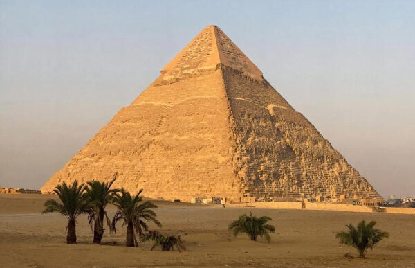 Пирамида Хеопса на фоне пустыни и пальм на закате в Гизе, Египет.