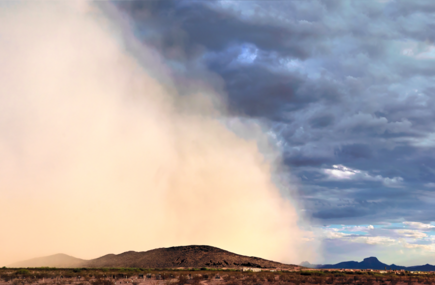 Пыльная буря в пустыне на фоне гор и облачного неба.