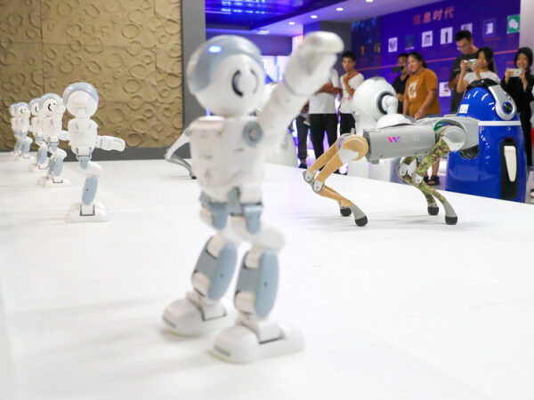 Роботы в танце на выставке технологий, люди в фоновом режиме наблюдают.