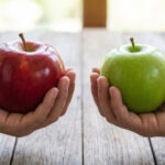 Сравнение красного и зеленого яблока в руках на деревянном фоне.