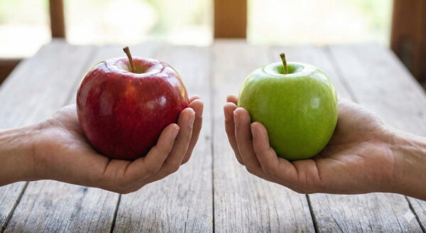Сравнение красного и зеленого яблока в руках на деревянном фоне.