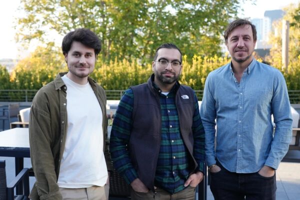 Три мужчины стоят на улице у зелёных деревьев, одеты в повседневную одежду.