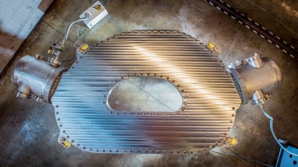 Металлическая деталь сложной формы на производственном полу, вид сверху.