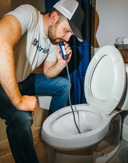 Мужчина проверяет унитаз с помощью камеры на гибком шланге в ванной комнате.