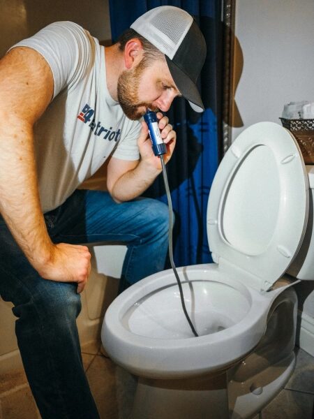 Мужчина проверяет унитаз с помощью камеры на гибком шланге в ванной комнате.
