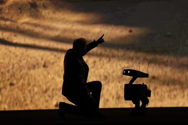 Силуэт человека и робота на фоне песчаной пустыни, человек указывает в сторону.