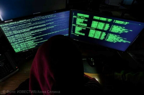 Программист за компьютером с двумя мониторами, показывающими код. Тёмный фон.