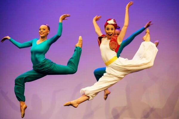 Два танцора в полете на сцене, исполняющие балет в ярких костюмах.