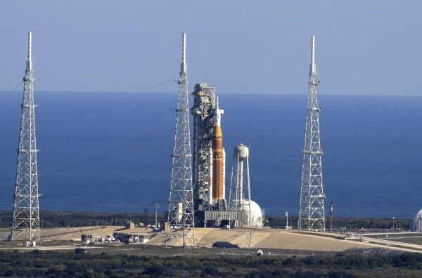 Ракета на стартовой площадке рядом с океаном, окружена башнями.