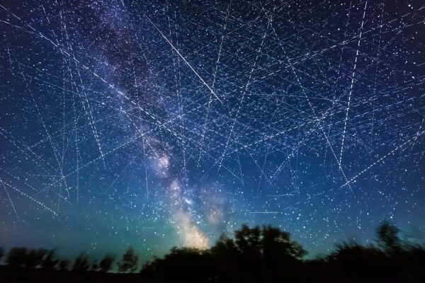 Ночное небо, Млечный Путь и следы спутников над лесом.