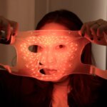 Девушка держит маску с красной подсветкой для ухода за кожей.