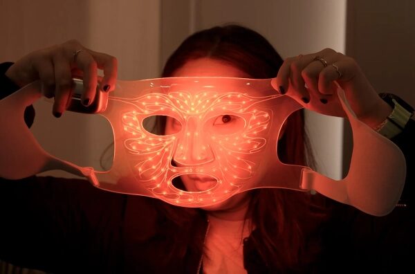 Девушка держит маску с красной подсветкой для ухода за кожей.