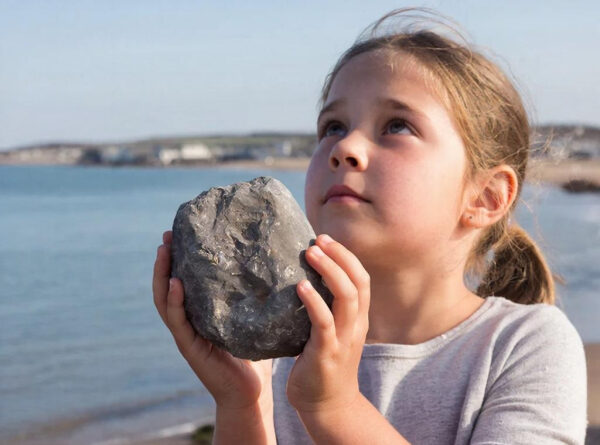 Ребенок держит камень на пляже, море на фоне.