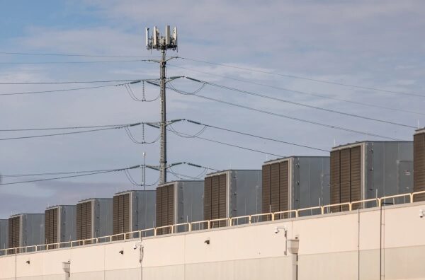 Промышленное здание с вентиляционными блоками и вышкой связи на фоне облачного неба.