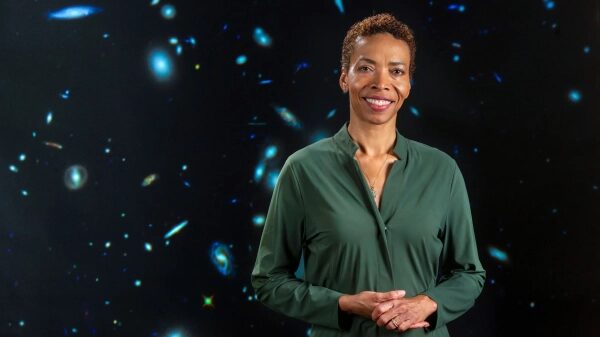 Женщина в зеленой рубашке на фоне звездного неба, улыбается.