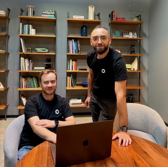 Двое людей за ноутбуком на фоне книжных полок в современной библиотеке.