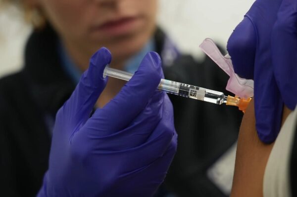 Медицинский работник в перчатках делает инъекцию пациенту в руку.