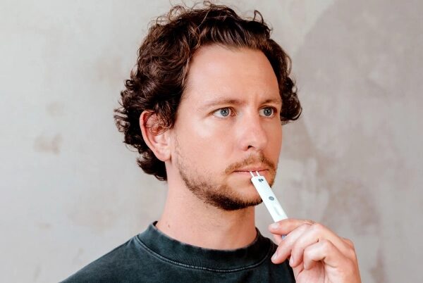 Мужчина держит белую зубную щетку на фоне стены.