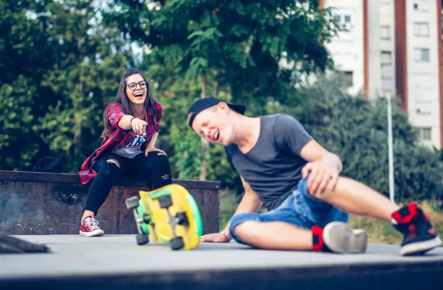 Скейтбордисты в парке, парень сидит на асфальте, девушка за ним смеется.