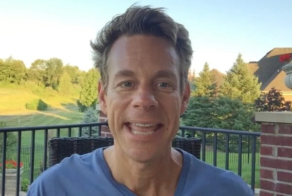 Мужчина на открытой террасе с зелёной растительностью на фоне, летний день.