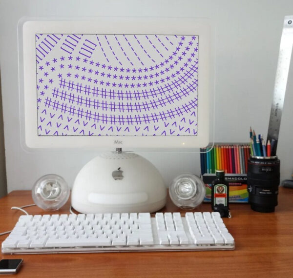 Старый компьютер iMac на столе с карандашами, динамиками и линейкой.