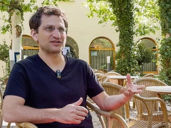 Адам Гриз дает интервью на открытом воздухе на конференции по долголетию.